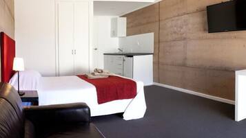 Une chambre d’hôtel moderne équipée d’un lit, d’un bureau, d’une chaise, d’une télévision et d’une armoire.