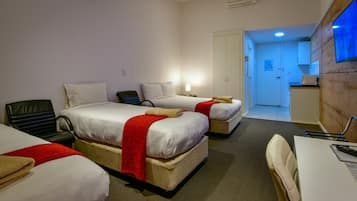 A hotel room with two beds, a desk, a chair, a small kitchenette, and a bathroom visible through an open door.