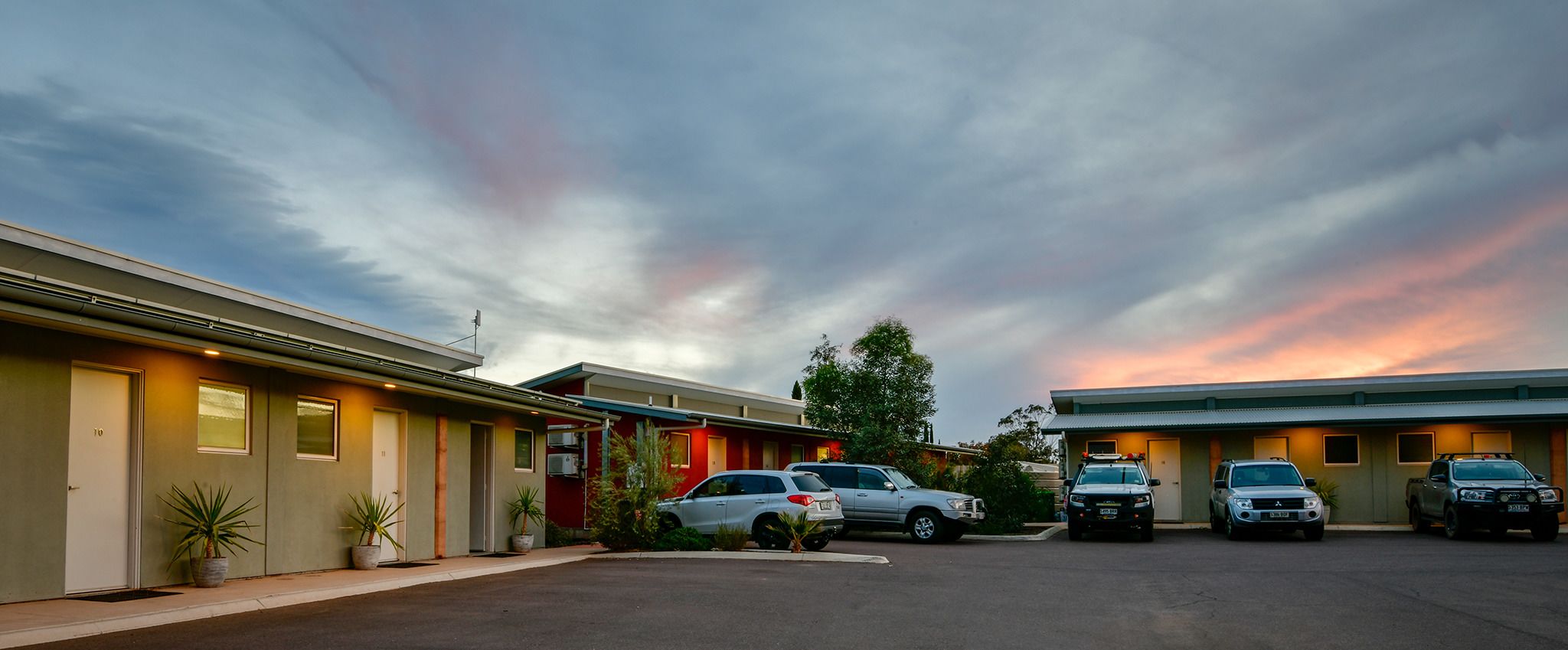 A motel with a row of rooms, a parking lot, and a sunset sky.
