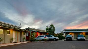 A motel with a row of rooms, a parking lot, and a sunset sky.