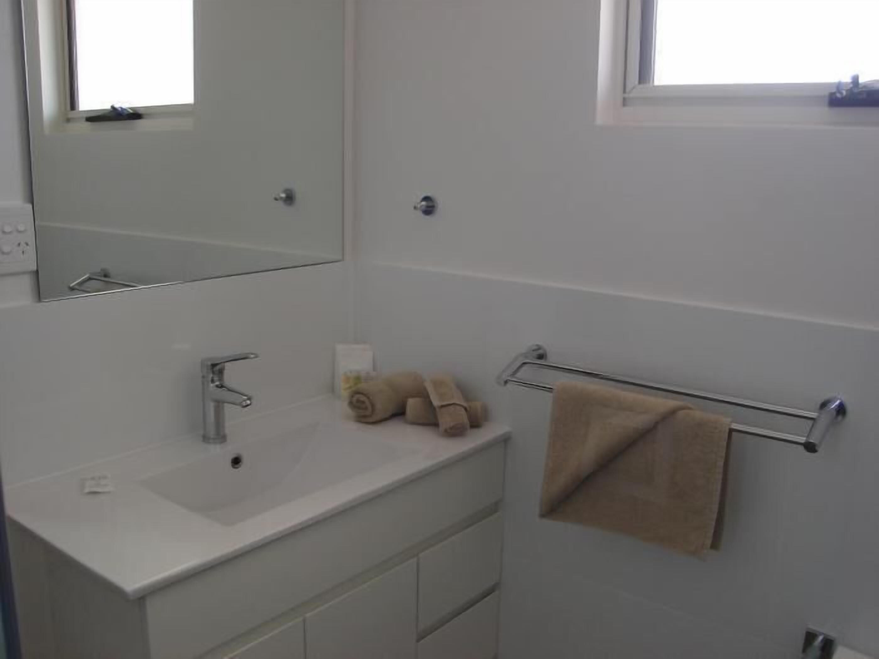 A bathroom with a white sink, a mirror, a towel rack, and a window.