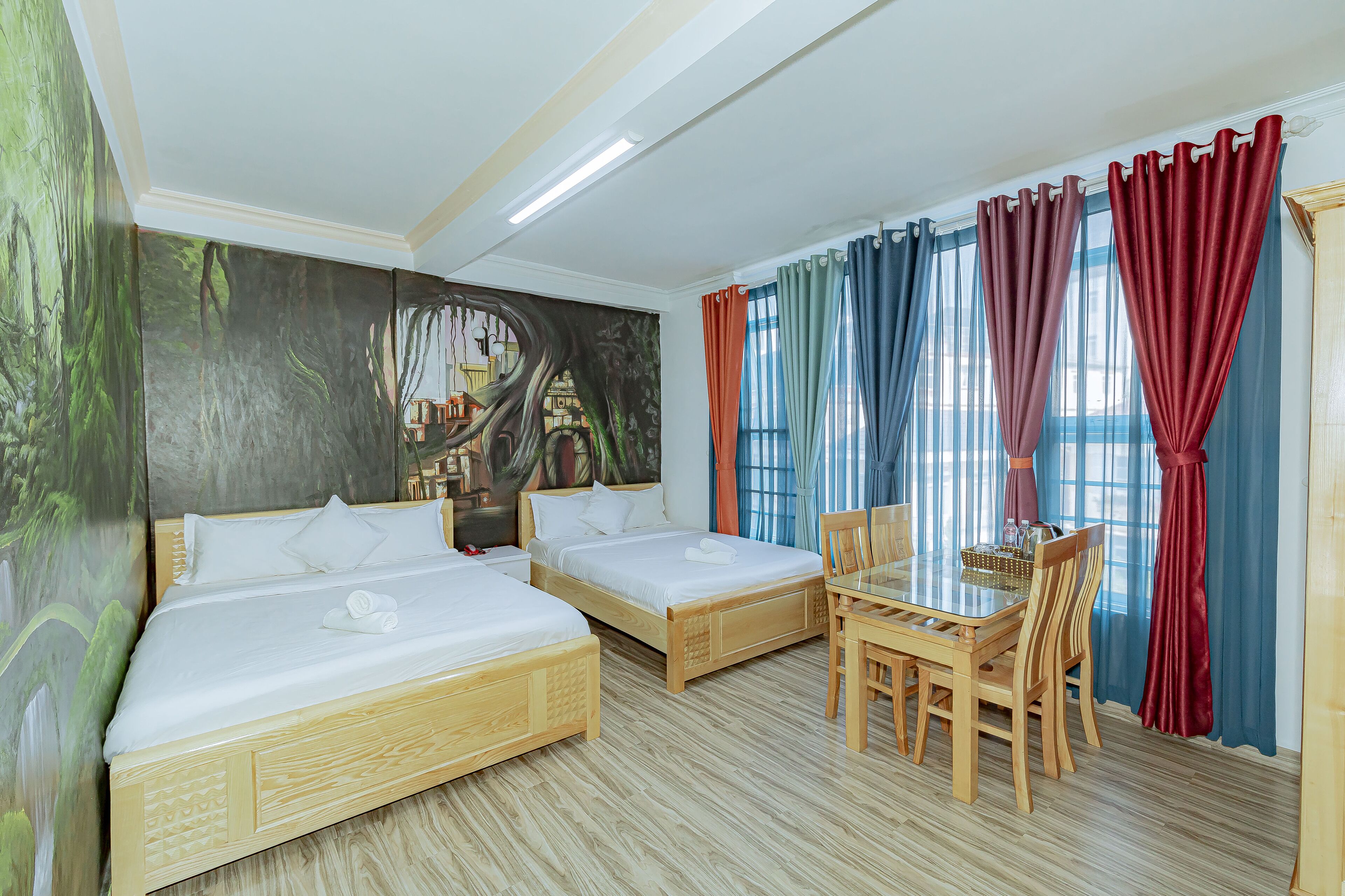 A hotel room with two beds, a dining table, and a mural on the wall.