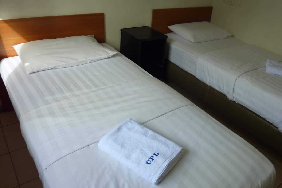 Two single beds with white linens, a black nightstand, and a folded towel with "GPL" on it.