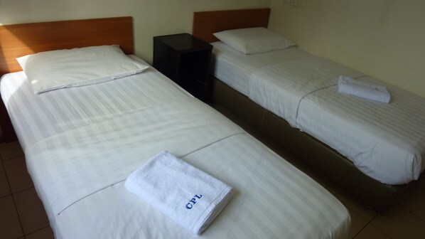 Two single beds with white linens, a black nightstand, and a folded towel with "GPL" on it.