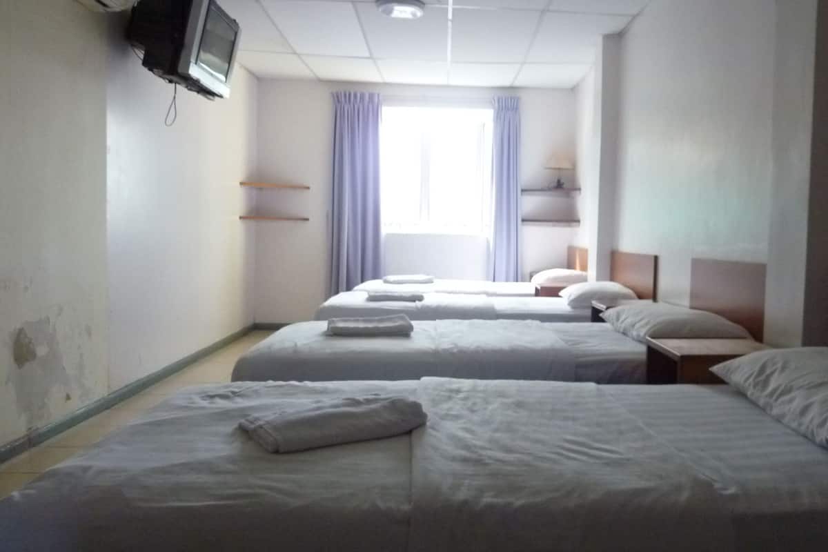 A hotel room with three single beds, a television on the wall, and a window with curtains.