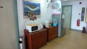 Une cuisine équipée d’un four à micro-ondes, d’une machine à café et d’un réfrigérateur. Il y a une affiche accrochée au mur et un extincteur fixé au mur.