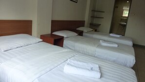 Une chambre d’hôtel avec trois lits simples, chacun équipé de draps et d’oreillers blancs. Une table de chevet en bois se trouve entre les lits.