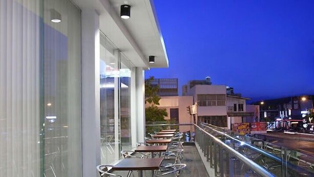 An outdoor seating area with tables and chairs, overlooking a street with buildings and a clear sky.