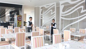 Un restaurant avec des tables blanches et des chaises à rayures, un coin bar et un mur décoratif orné de motifs abstraits.