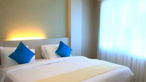 Une chambre d’hôtel avec un lit bien fait, une tête de lit et une fenêtre ornée de rideaux légers.