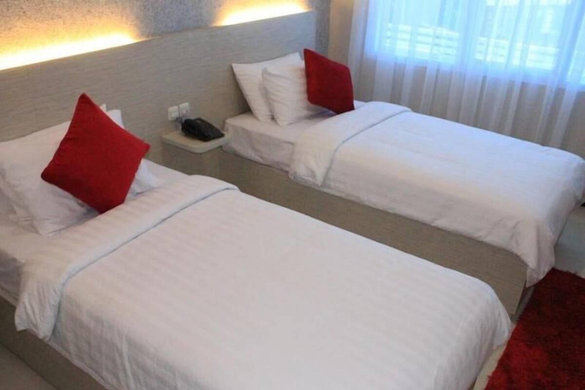 Une chambre d’hôtel avec deux lits, chacun doté de draps blancs et d’oreillers rouges, une table de chevet avec un téléphone et une moquette rouge.