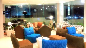 Un espace de détente moderne avec des canapés et des fauteuils, de grandes fenêtres offrant une vue sur la ville et une cloison en verre.