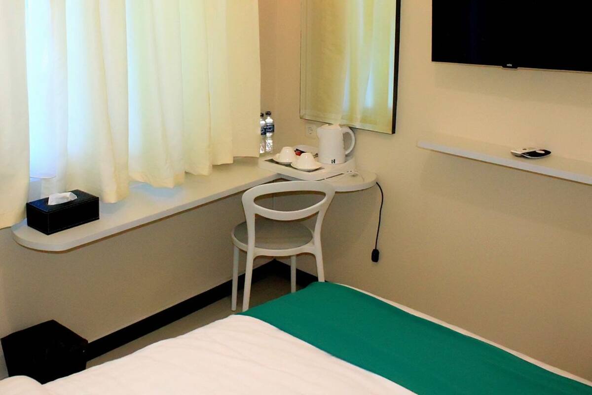Une chambre d’hôtel comprenant un lit, un bureau avec une chaise, une télévision et une fenêtre avec des rideaux.