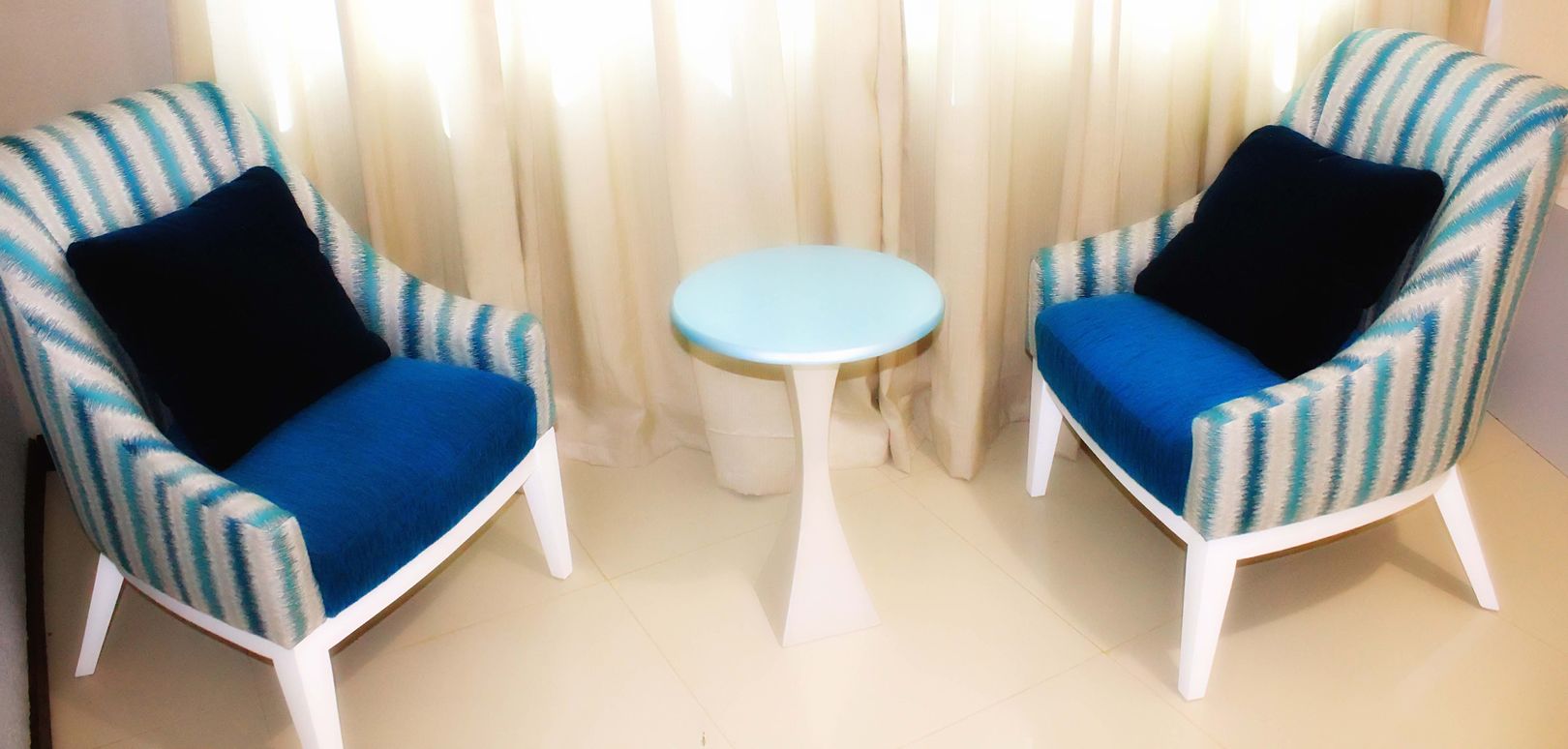 Two striped armchairs with blue cushions and black pillows, a small round table, and a white floor.