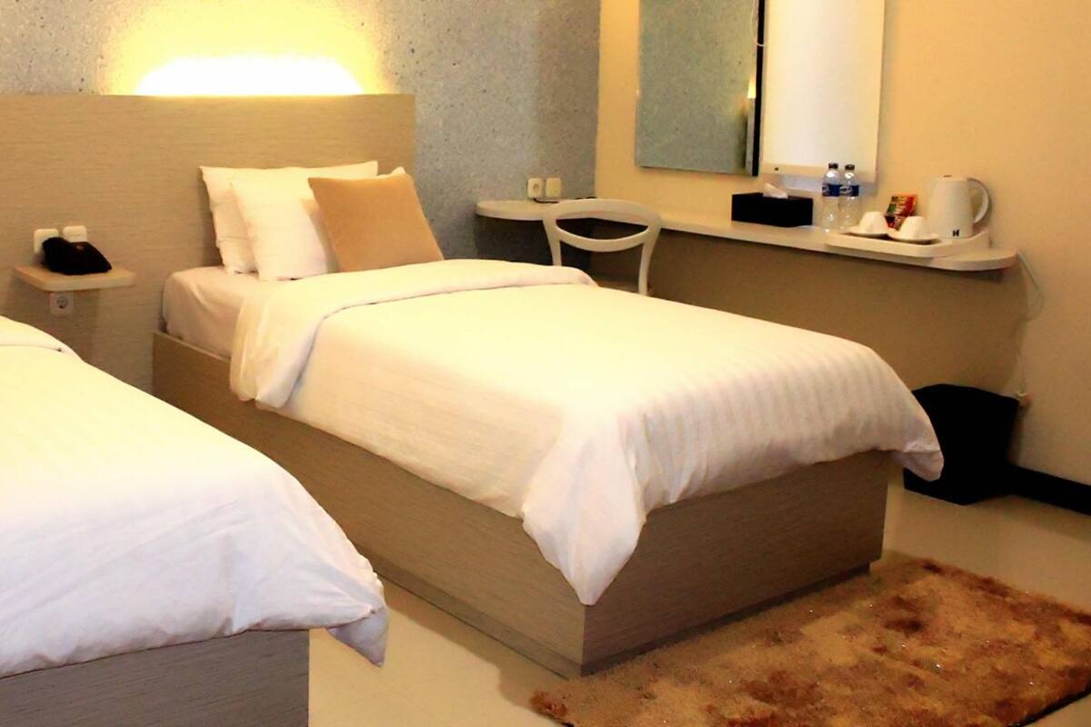 Une chambre d’hôtel avec deux lits simples, une petite table, une chaise, un miroir et une table de chevet avec un téléphone et une lampe.