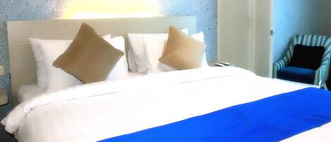 Habitación de hotel con cama, almohadas, una manta azul, una silla y una pared con textura.