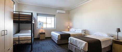 Habitació d'hotel amb un llit superposat, dos llits individuals, un ventilador de sostre, un aparell d'aire condicionat, una finestra amb vista i un escriptori amb una làmpada.