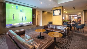 A hotel lobby with leather sofas, round tables, a large screen displaying a sports game, and a bar area in the background. - Toongabbie Hotel (Toongabbie)