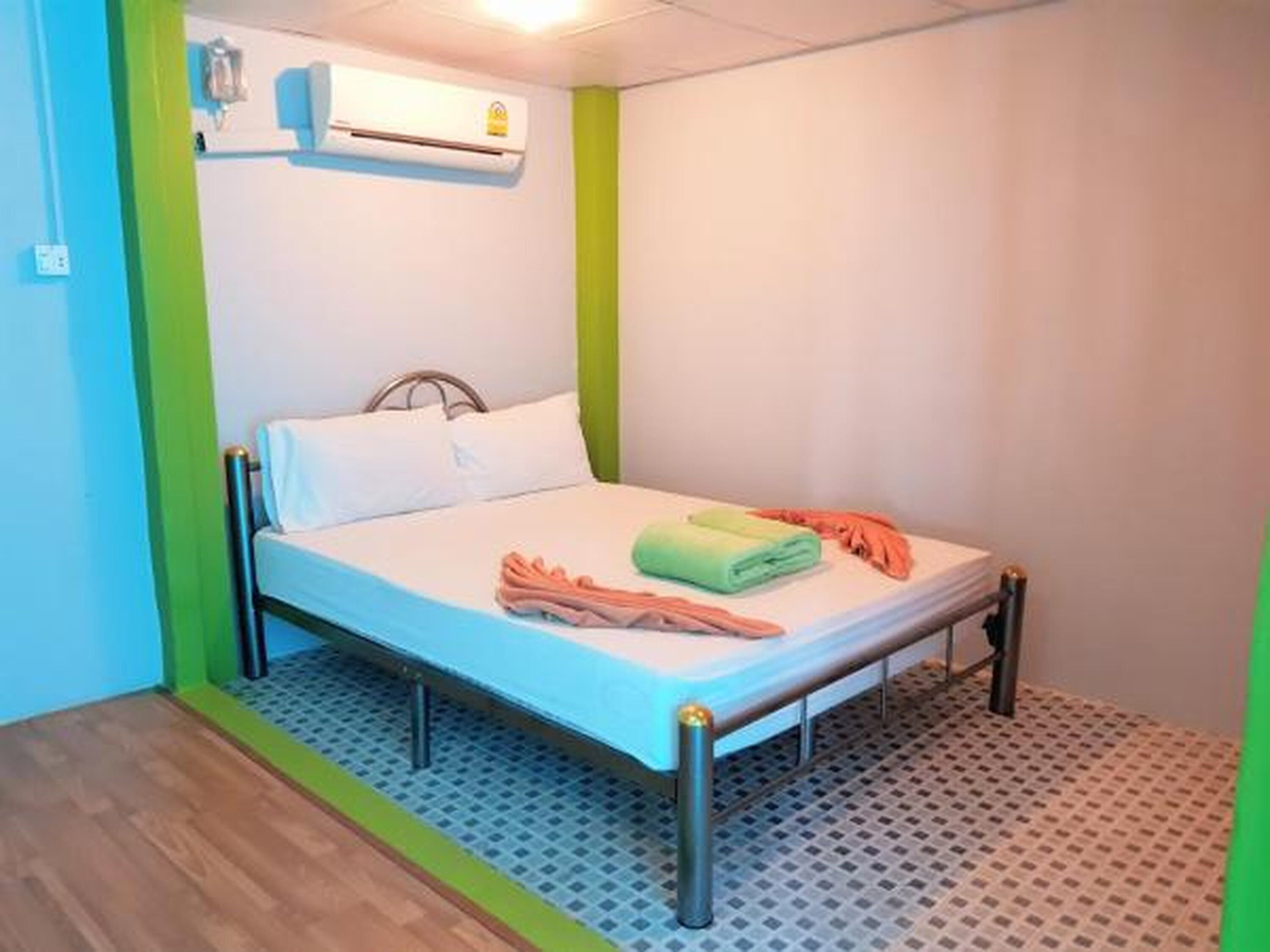 A single-bed room with a metal frame, a white mattress, and a green towel.