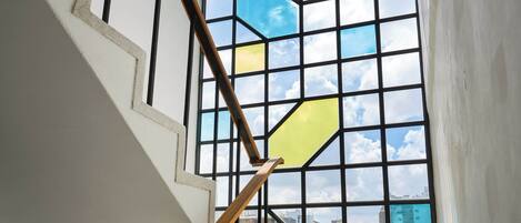 A staircase with a geometric stained glass window, a wooden handrail, and a hanging light fixture.