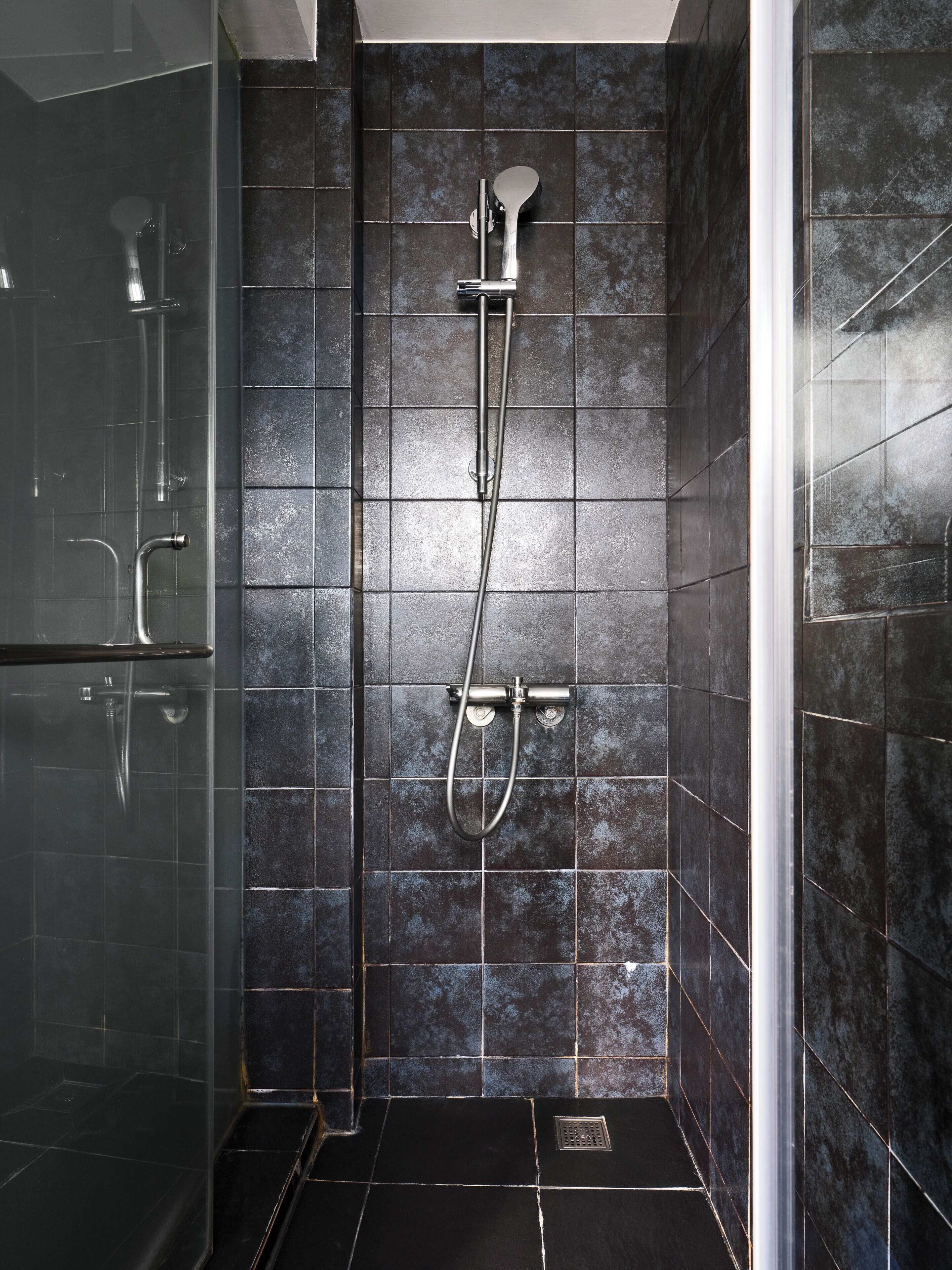 Un baño moderno con baldosas oscuras, cabina de ducha de cristal y ducha visible.