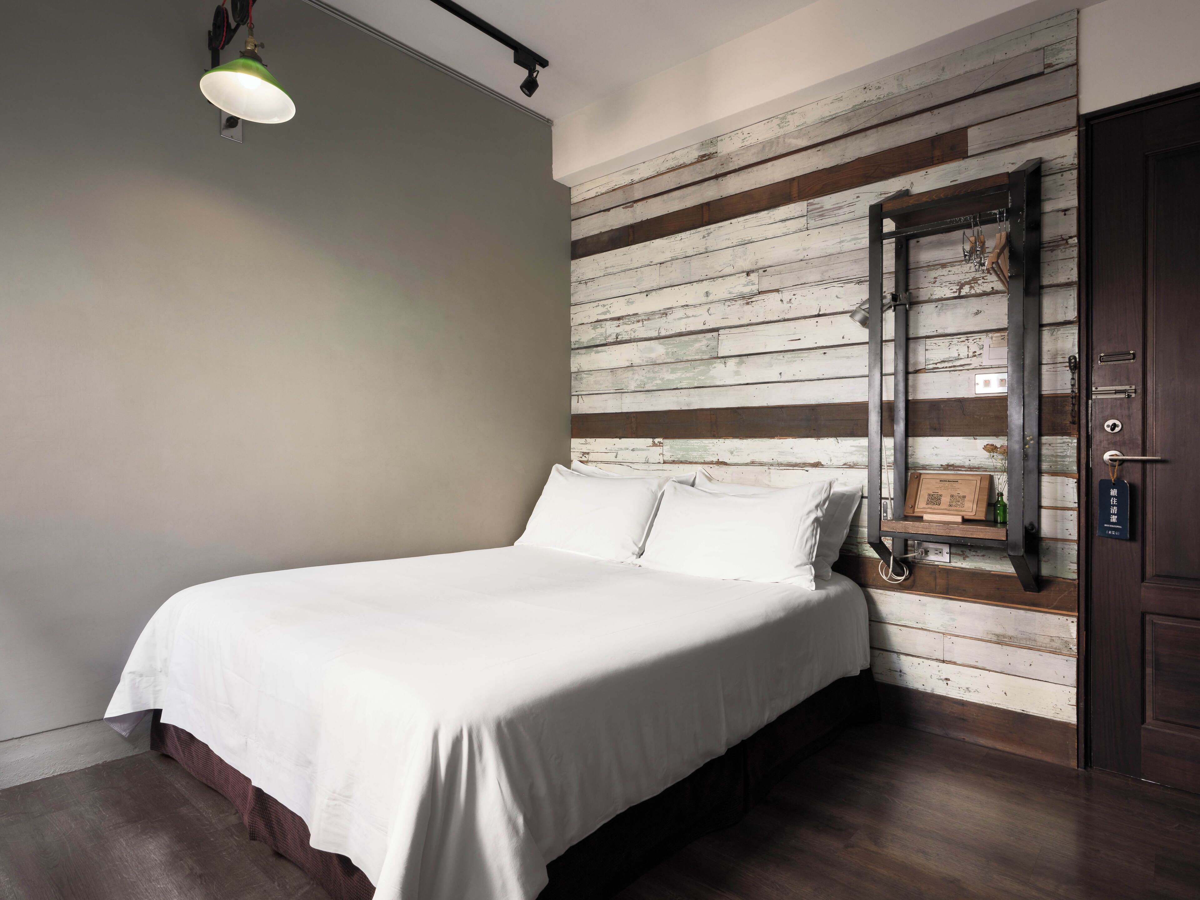 A bedroom with a bed, a wooden wall panel, a door, and a hanging light fixture.
