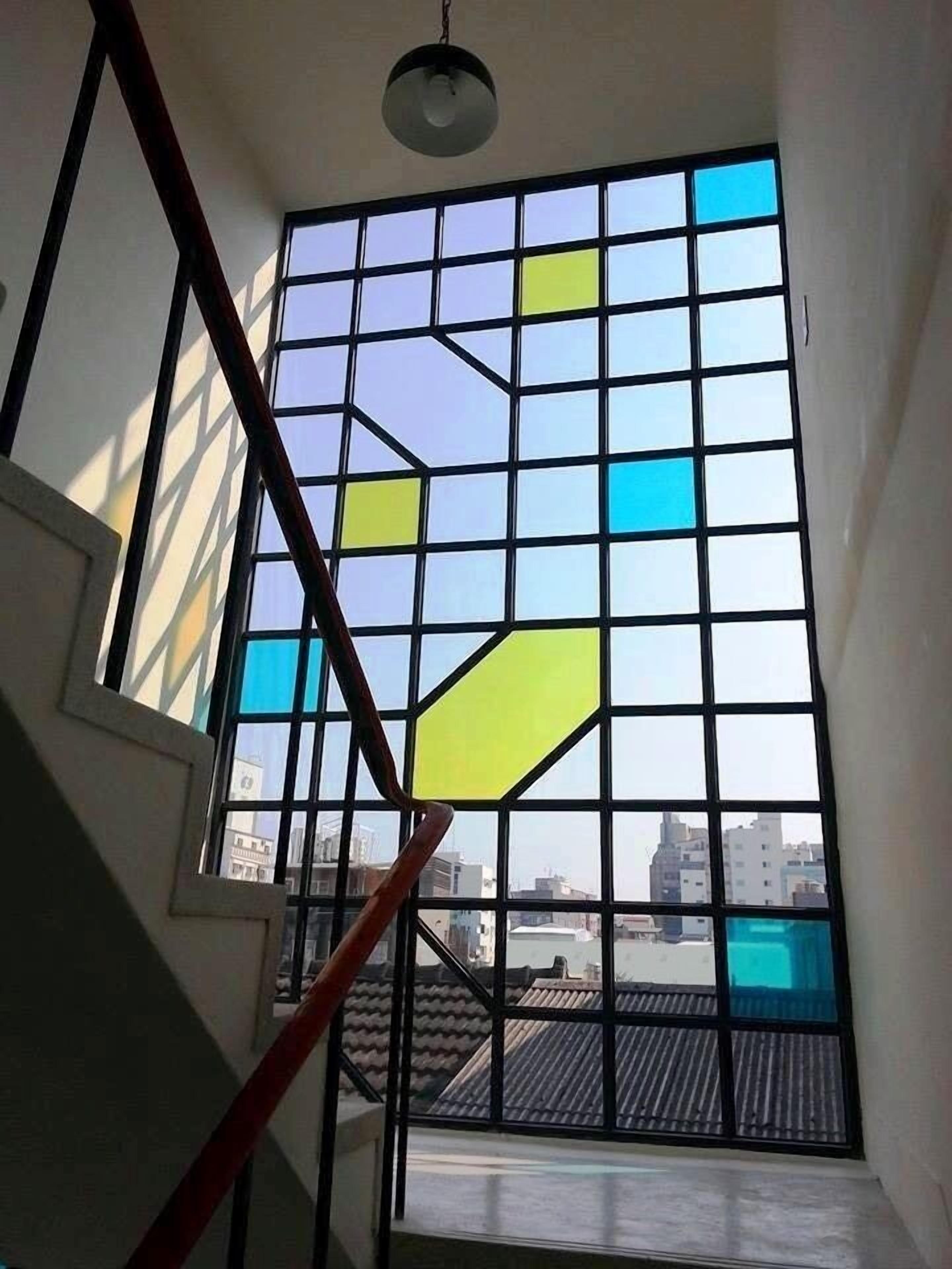 Een trap die leidt naar een kamer met een groot raam met geometrisch mozaïekglas.