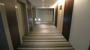 Un passadís d'hotel amb moqueta rayada, portes i una làmpada al sostre.