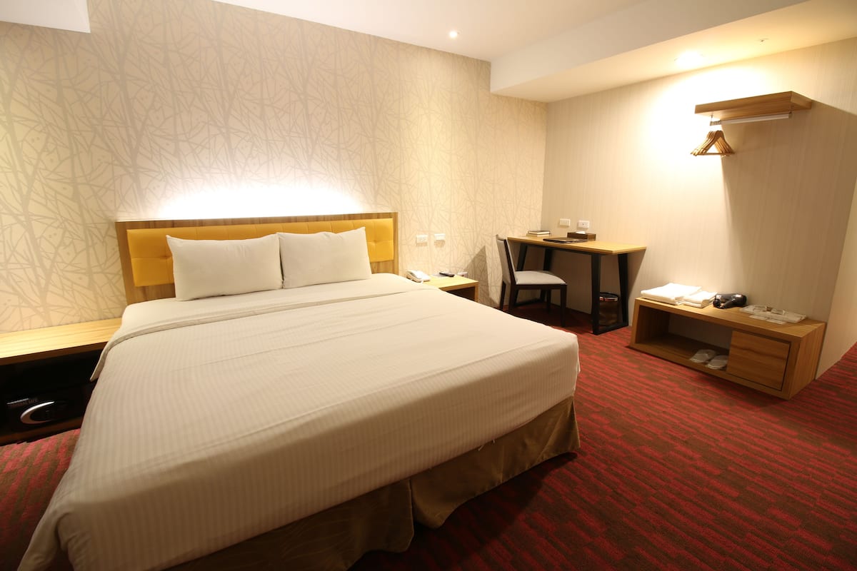 Quarto de hotel com uma cama grande, uma escrivaninha e uma cadeira.