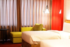 Una habitación de hotel con una cama, un sillón amarillo, una mesita pequeña y una pared decorada en rojo.