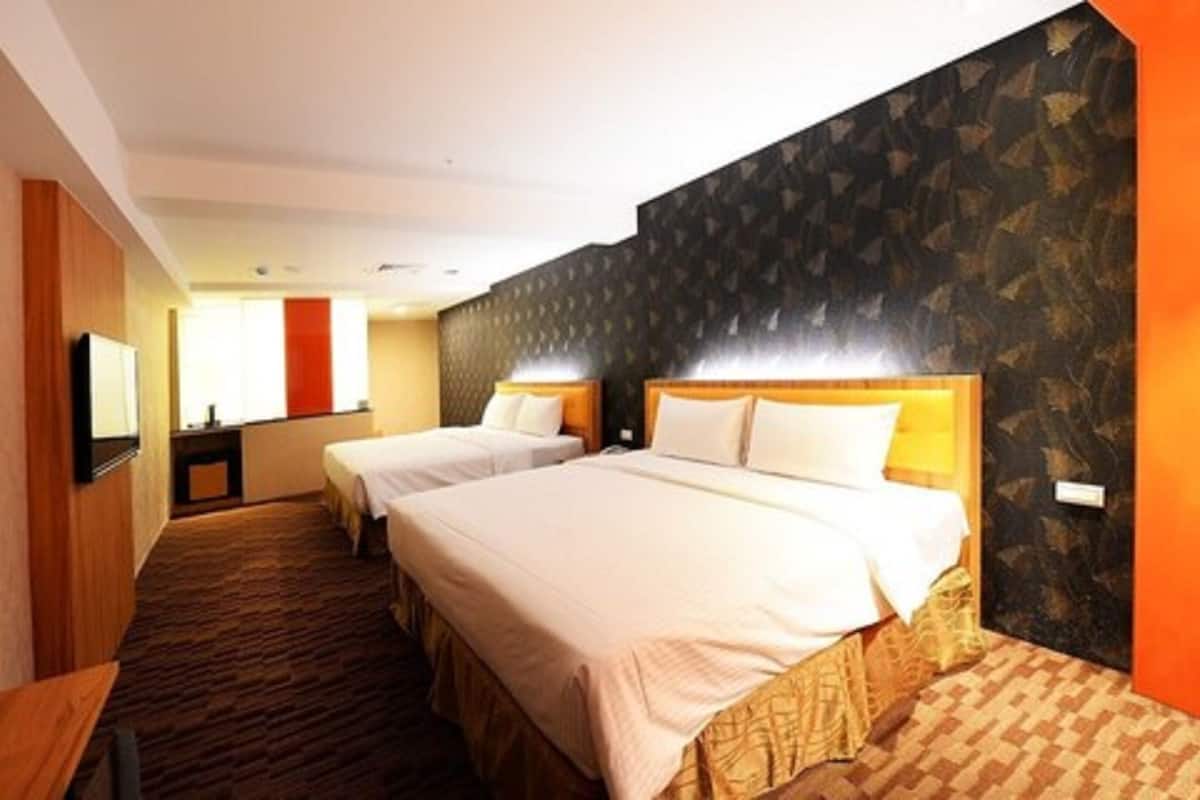 Quarto de hotel com duas camas, televisão, escrivaninha e banheiro.