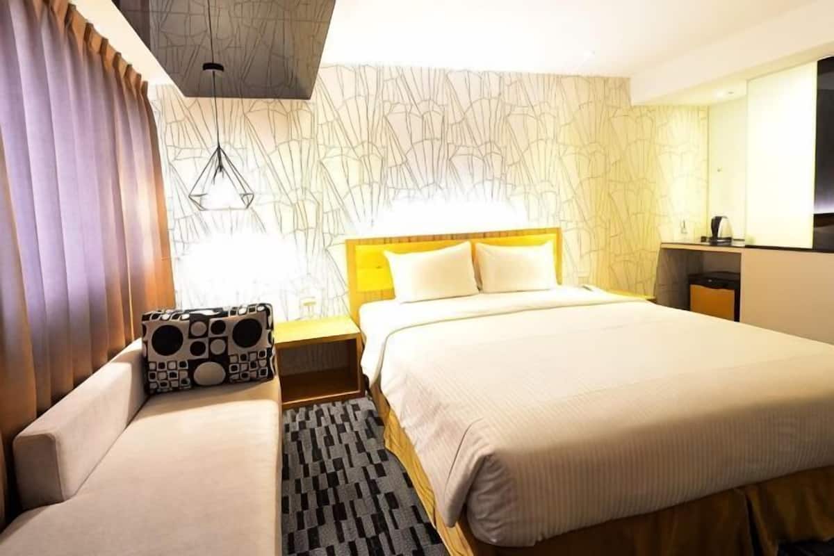 Quarto de hotel com uma cama grande, um sofá, um tapete estampado, uma cabeceira de madeira e uma parede com design único.