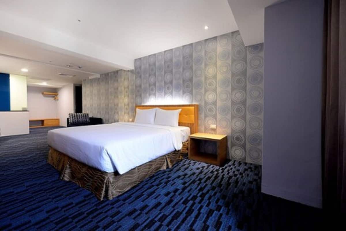 Quarto de hotel com uma cama grande, uma mesinha de cabeceira, parede com um desenho circular e piso coberto por carpete.