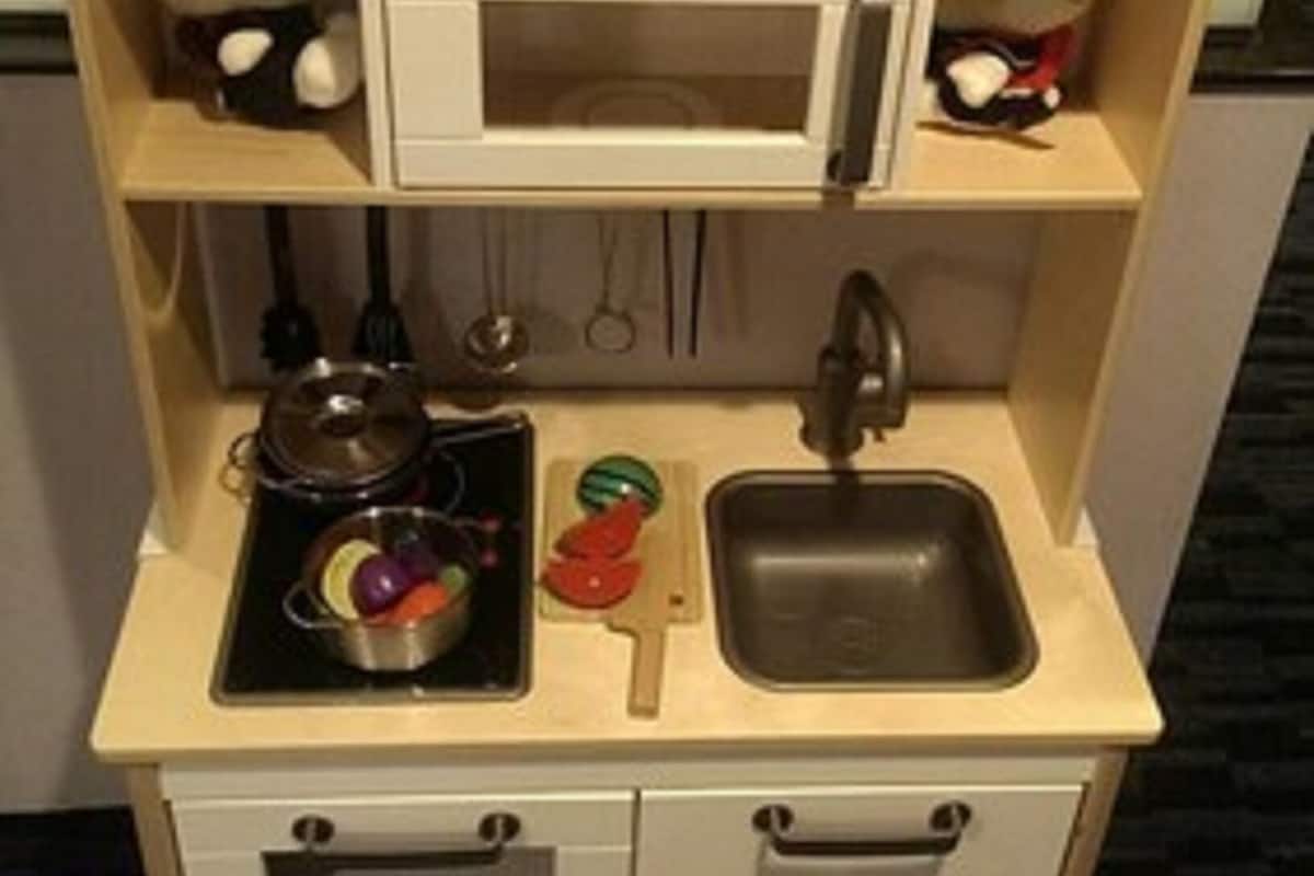 Uma cozinha de brinquedo para crianças, com micro-ondas, pia e gavetas.