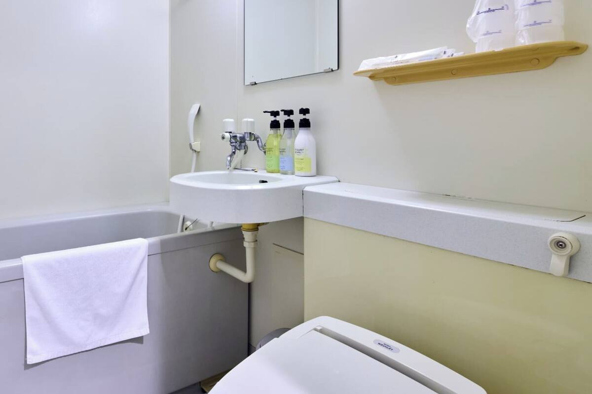 Une salle de bain avec une baignoire, un lavabo et des toilettes. On trouve des articles de toilette sur le lavabo et une serviette est accrochée à la baignoire.