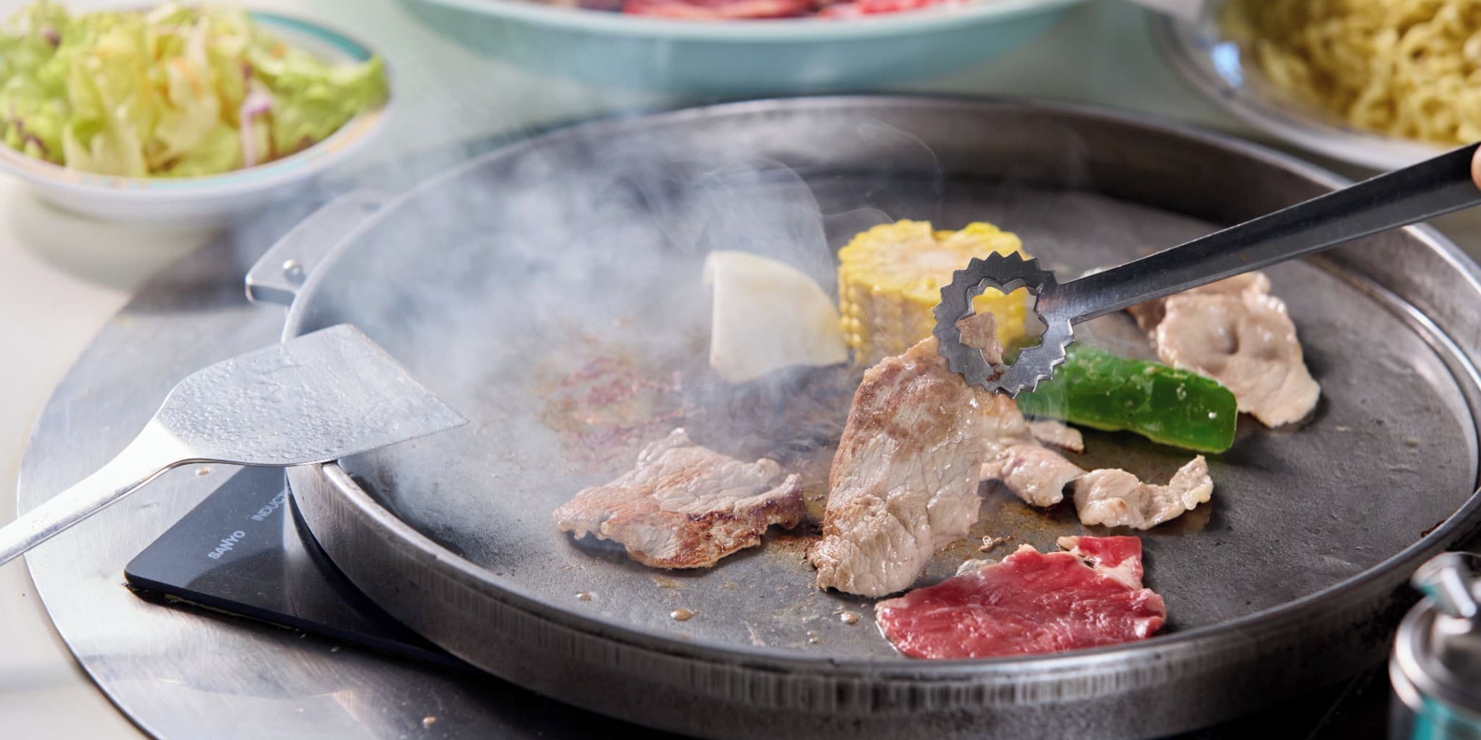 A hot plate with various meats and vegetables being grilled.