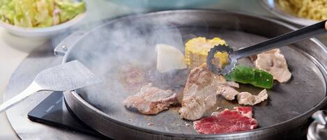 A hot plate with various meats and vegetables being grilled.