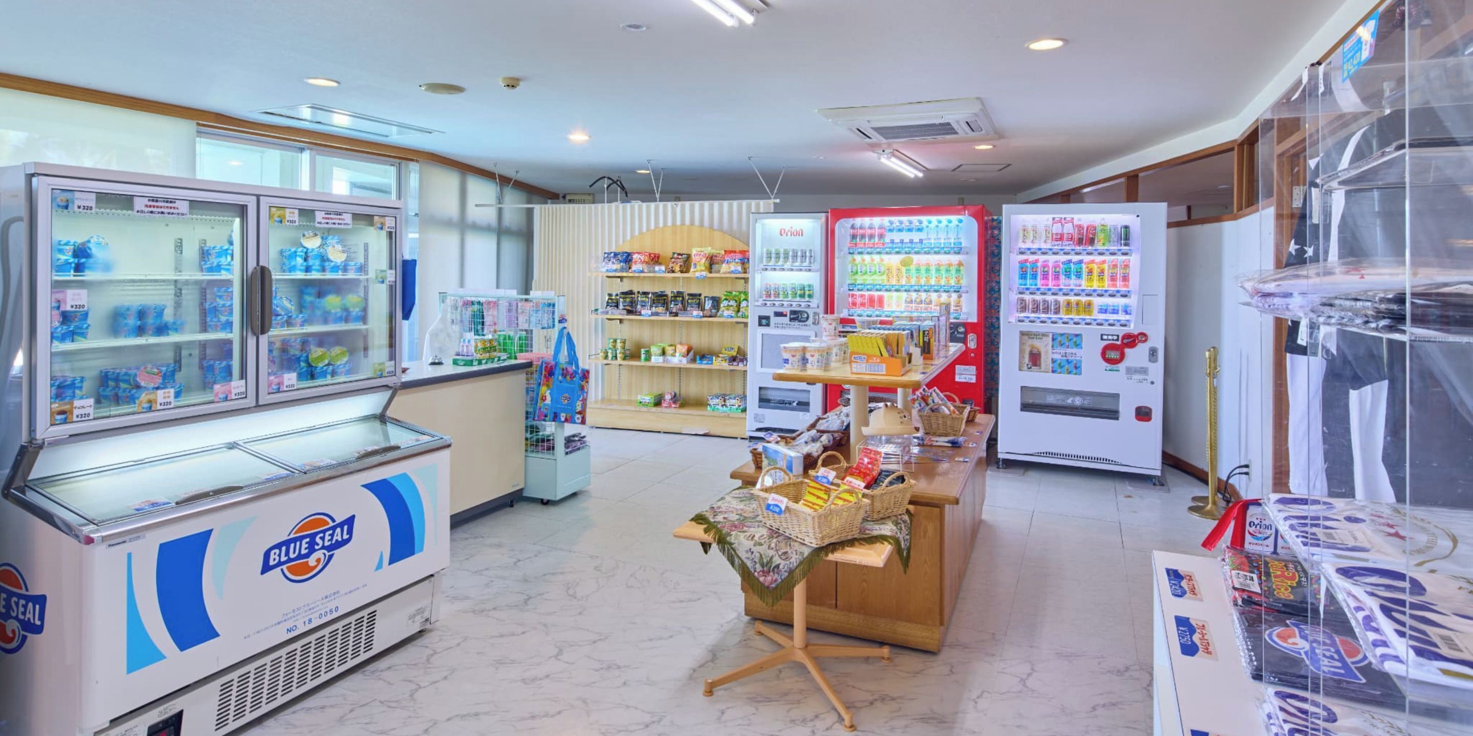 A convenience store with refrigerated freezers, shelves stocked with snacks, and vending machines.