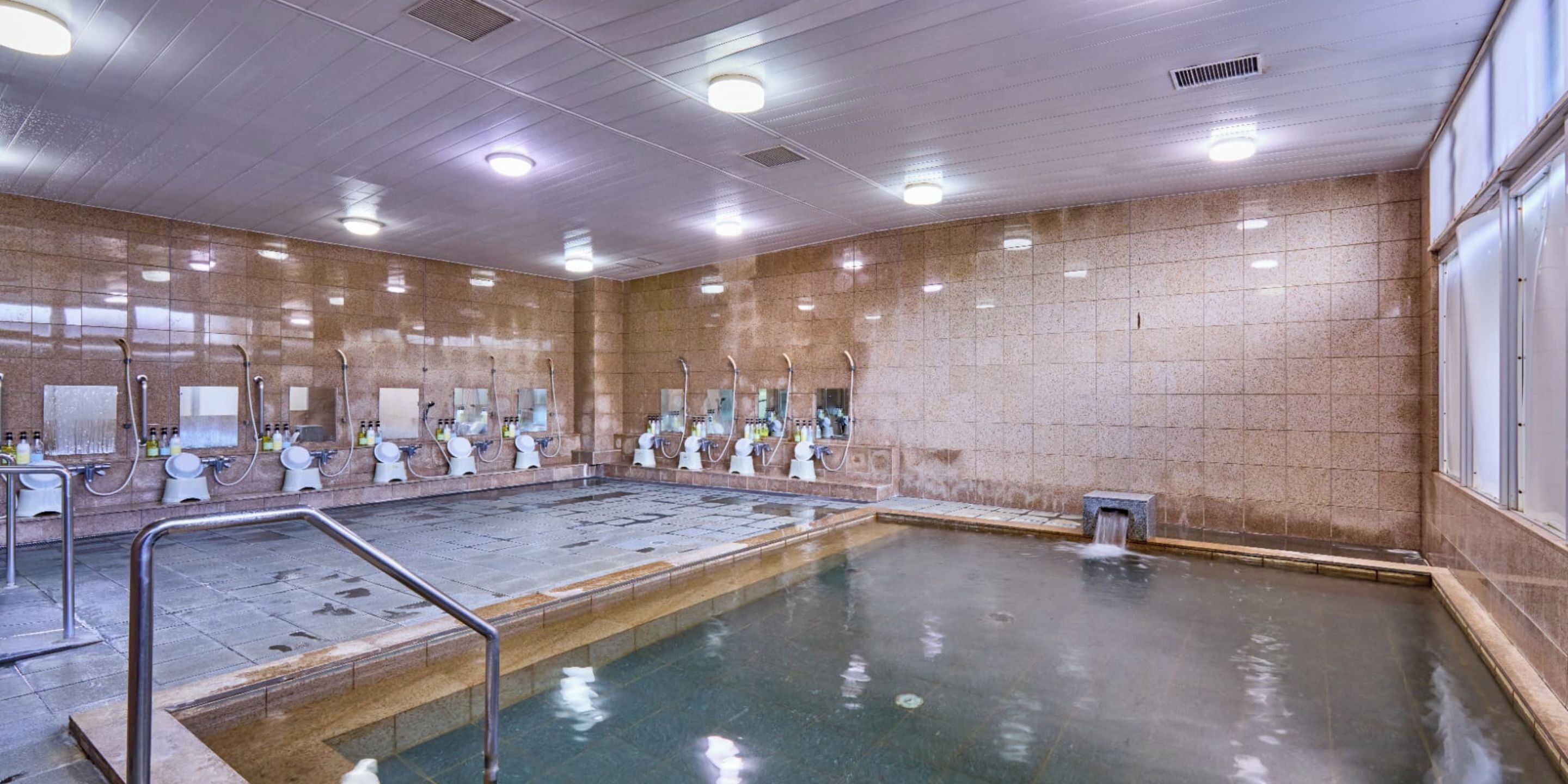 A large indoor swimming pool with multiple shower areas and a tiled wall.