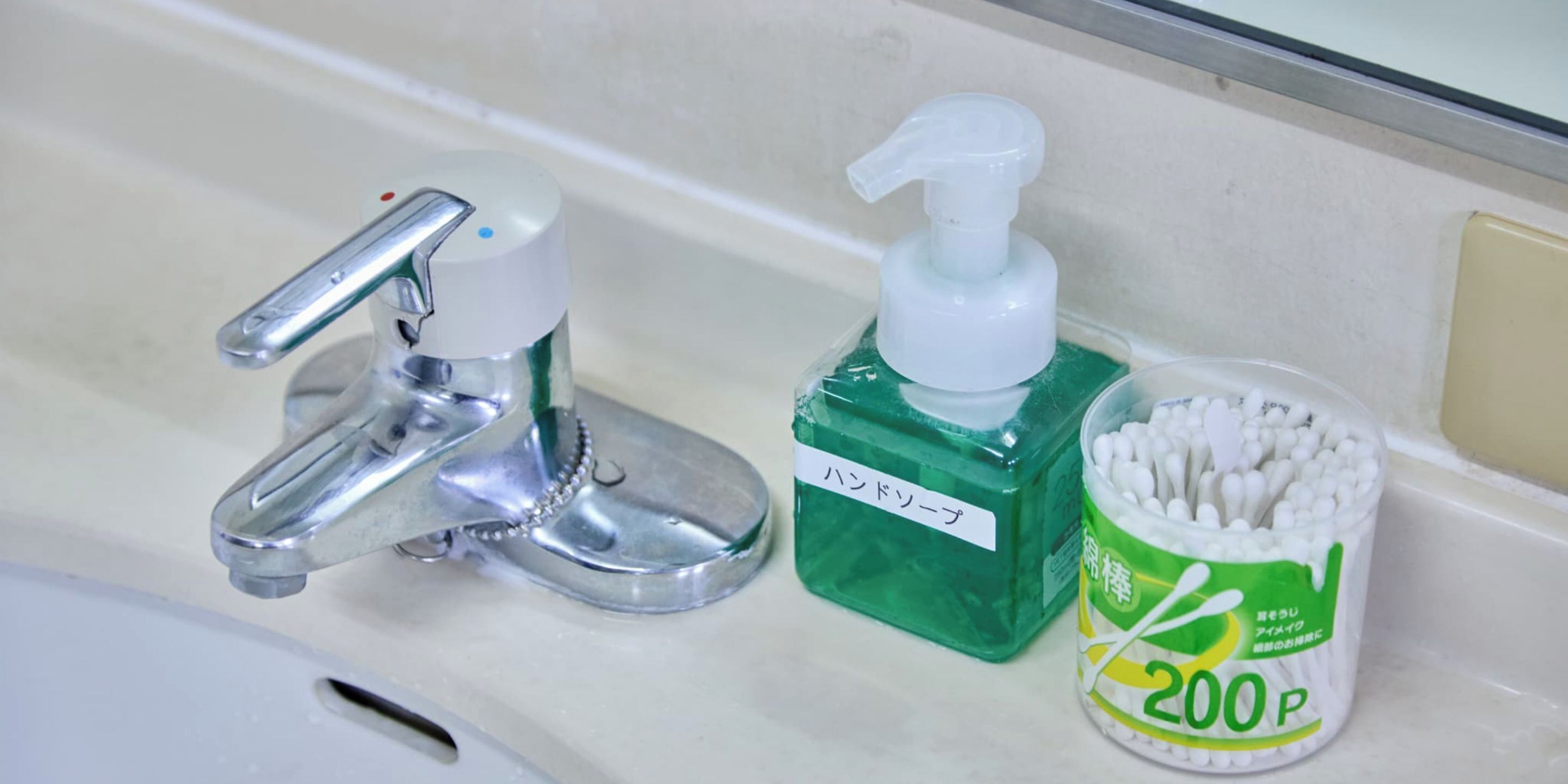 Un lavabo de salle de bain avec un robinet chromé, un distributeur de savon vert et un récipient rempli de cotons-tiges.