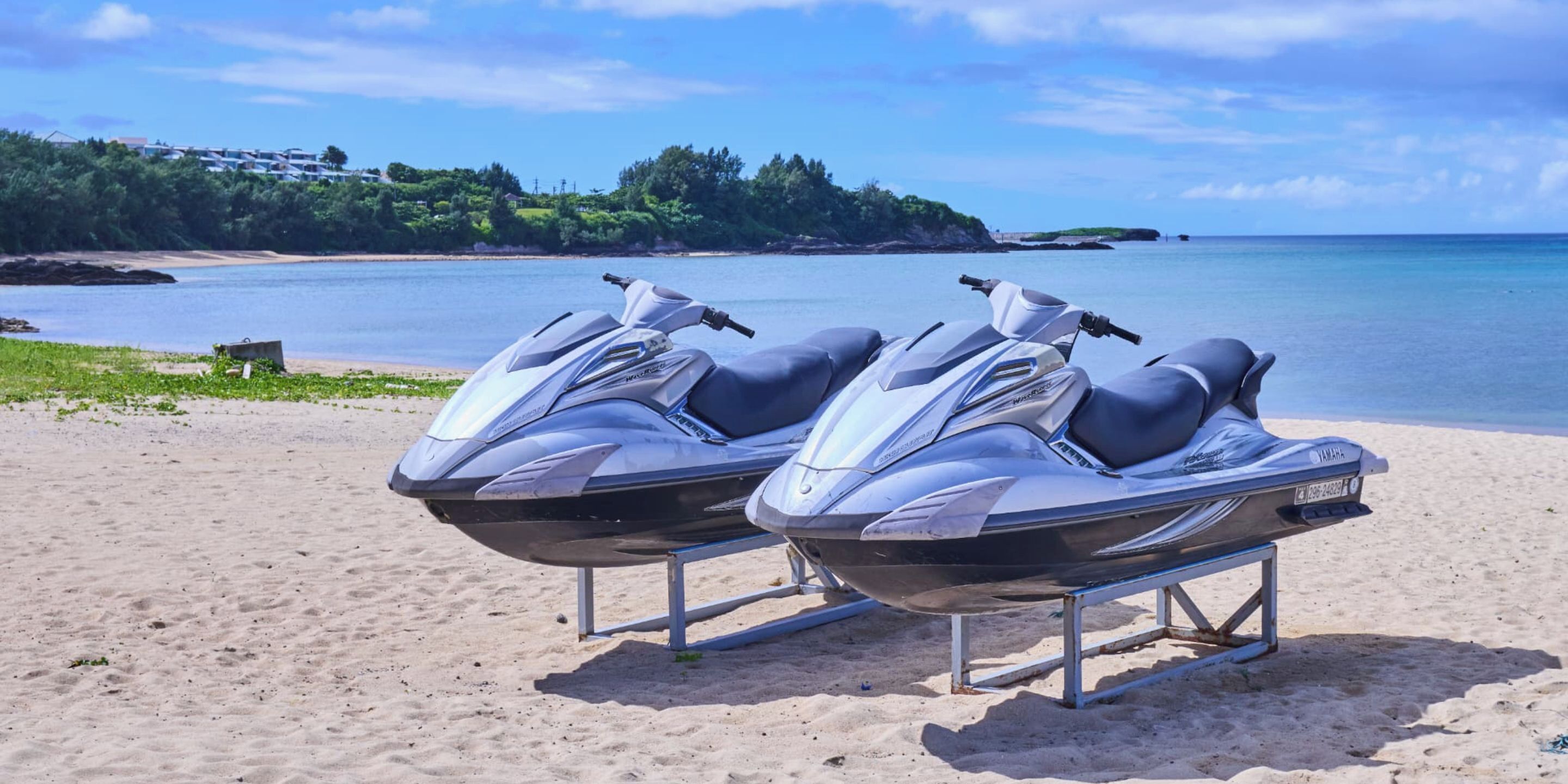 Two jet skis on a beach with a view of the ocean and a distant shoreline.