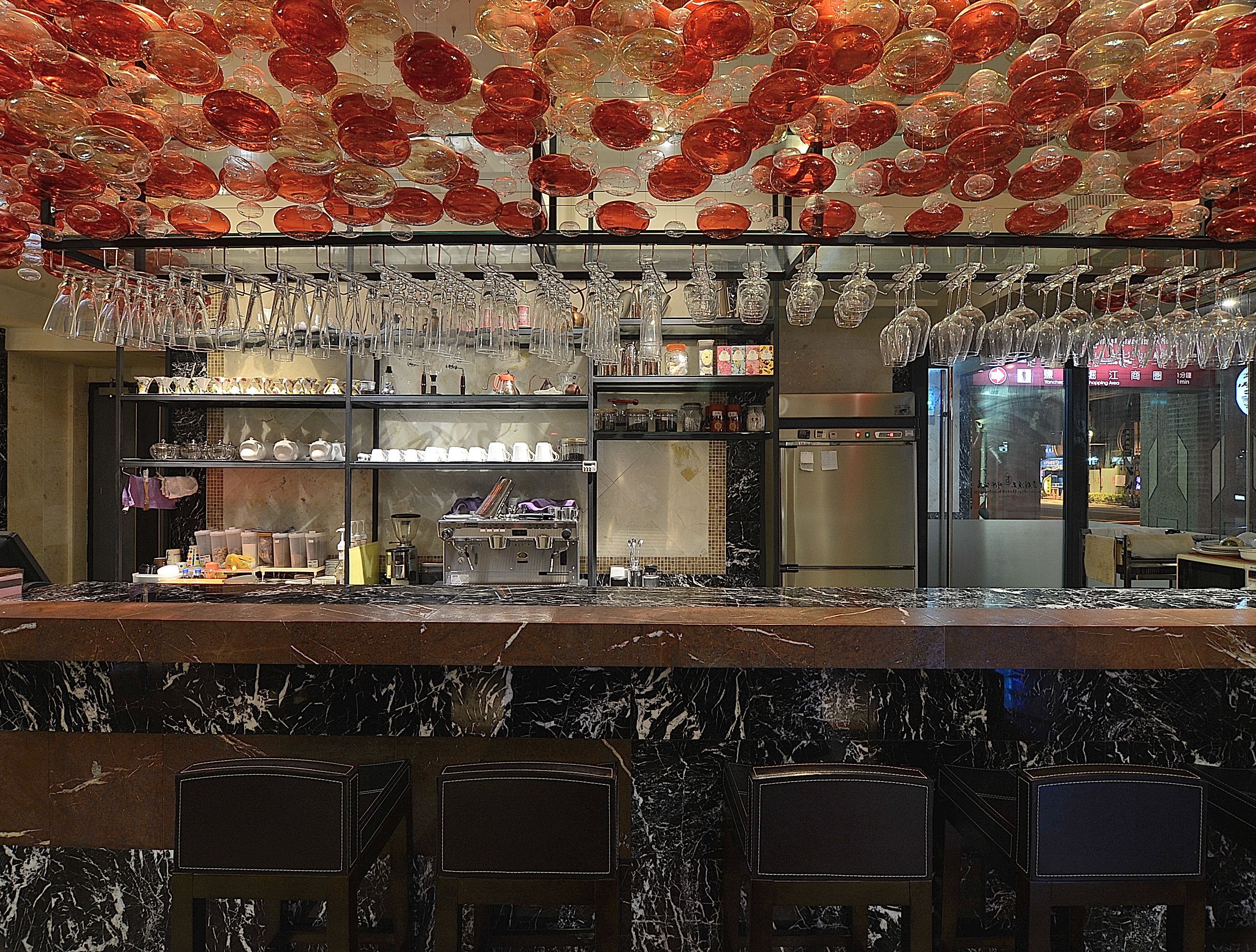 A bar area with a marble countertop, multiple shelves with glassware, and a refrigerator.