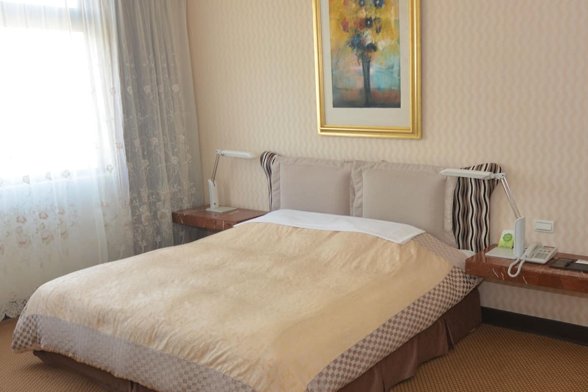 A hotel room with a large bed, a bedside table with a lamp, a telephone, and a painting on the wall.