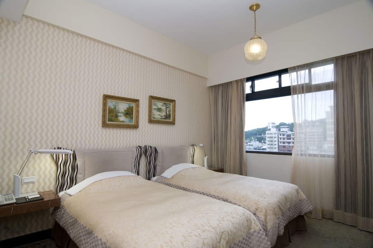 A hotel room with two beds, a desk with a lamp, a telephone, and a window with curtains.