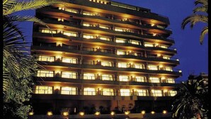 A multi-story hotel with balconies, a well-lit entrance, and palm trees in the foreground. - Hotel Harvest Ito (Ito)