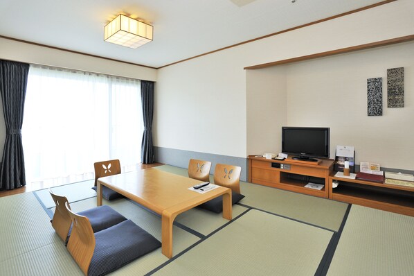 Una habitación tradicional japonesa con suelo de tatami, una mesa de madera baja, dos esteras de tatami, un televisor y un mueble con un pequeño estante.