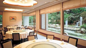 A restaurant with round tables, a central water feature, and a view of a waterfall through large windows. - Hotel Harvest Ito (Ito)