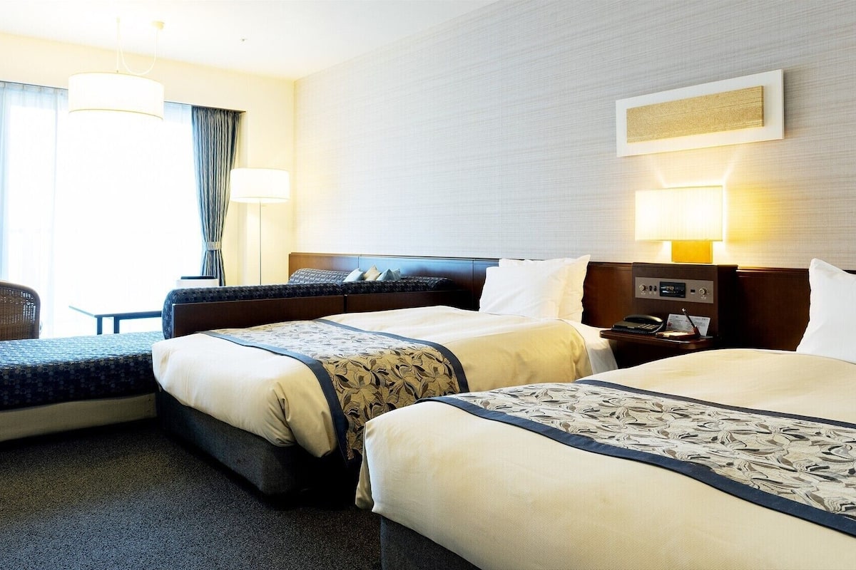 Una habitación de hotel con dos camas, una silla, un escritorio con teléfono y una lámpara.