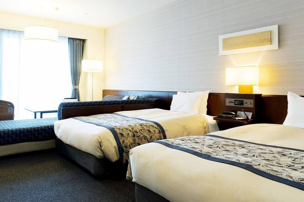 Una habitación de hotel con dos camas, una silla, un escritorio con teléfono y una lámpara.