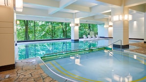 Une piscine intérieure avec des parois en verre transparent, un sol en pierre et des chaises longues au bord de la piscine.